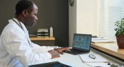 Physician Working on Laptop With Group of Doctors on Screen